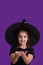 A girl in black clothes and a witch's cap on violet background