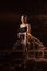 Girl in black dress on chair in water in a small pool, drops of water and dark background