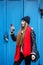 A girl in a black hat and a black jacket against a blue wall holds a phone, stylish and youthful
