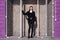 Girl in black jacket and jeans standing near technological room with metal grid door