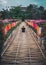 A girl in a black T-shirt is sitting with her back to the camera on a bamboo path decorated with bright Thai umbrellas