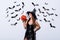 Girl in black witch Halloween costume holding carved spooky pumpkin near white wall