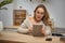 Girl blogger in glasses, beige sweater. Holding tablet, sitting in kitchen at table with notebooks, smartphone, plastic