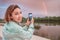 Girl blogger photographs and shoots video content for her social networks - a bright rainbow stretches over the river