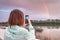 Girl blogger photographs and shoots video content for her social networks - a bright rainbow stretches over the river