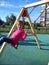 A girl with blond hair, dressed in a pink blouse, swings heavily on a swing and smiles. Green rubber shockproof pad on new