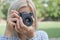 Girl blonde with a camera focuses in the park