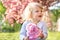 girl blonde plays with a sprig of sakura in a flowered sakura garden