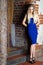 Girl in blue dress posing against brickwall.