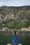 A girl in a blue dress stands with her hands up on the pier against the backdrop of the Bay of Kotor in Montenegro. Nice and cozy