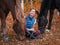 A girl in a blue jacket lies next to the horse and laughs. Golden autumn background