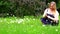 A girl in a blue sarafan collects wild flowers sitting on green grass