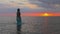 A girl in a blue swimsuit and a bright pareo posing against the background of a sunset in estuary with transparent water