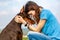 A girl in a blue T-shirt and a brown-and-tan doberman dobermann dog sit forehead to forehead against the sky. Horizontal