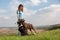 A girl in a blue T-shirt stands on a hill and feeds her Doberman Dobermann and a border collie dogs with treats on a