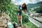 A girl in a blue top and a denim skirt walks cautiously along the stones against the backdrop of mountains