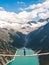 Girl in blue tshirt and a yellow hat sitting on a suspension bridge above the Alps. Freedom and adventure concept. Touristic