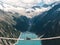 Girl in blue tshirt and a yellow hat sitting on a suspension bridge above the Alps. Freedom and adventure concept. Touristic