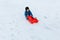 Girl in blue winter clothes pushing up the snowy hill the red sled