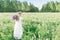 A girl with a bouquet of flowers over her shoulder in a white dress and a flower wreath walks back along the flower