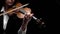 Girl bows a violin in a dark room. Black background. Close up