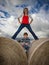 Girl and boy pose on round hay bales under a cloudy blue sky.