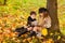 Girl and boy sit under a tree and read a book together in autumn sunny park, children sit in leaves
