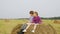 Girl and boy teenagers sitting on haystack at harvesting field. Happy boy and girl reading book on hay stack at autumn