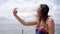 Girl with braces on her teeth, young female in swimsuit photographed on mobile to waterfront ocean, selfi of girl in