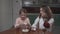 Girl breaks a chicken egg in bowl sitting at the table in the kitchen with her older sister