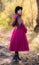 Girl in a bright crimson coat walking in forest sunny autumn day