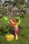A girl in bright multicolored clothes and rubber boots hangs clean laundry on a clothespin under a tree in the garden.