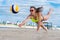 A girl in a bright yellow bathing suit stretches and falls to catch a ball while playing beach volleyball against the