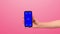 The girl brings her hand with a modern phone with a blue screen chromakey on a pink background