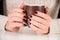 Girl with brown nails manicure holds cup of coffee on desk