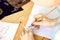 A girl calligrapher paints pen on white paper behind her working wooden table.