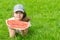 A girl in a cap, lies on the green grass and holds a piece of watermelon, there is a place for inscription