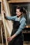 Girl carpenter with a tape measure on a background of wooden pieces in workshop.