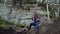 A girl in the casual clothes climbs a thick fallen tree and sits on it against the background of the mountain