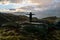 Girl celebrates with hands out in the mountain during heavy rain weather and sunbeams over mountain tops in the background.