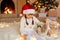 Girl child celebrates Christmas with Pekingese dog at home near Christmas tree, sitting on floor, hugging her pet and looking at