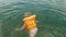 Girl child in an orange life jacket is bathing in the water