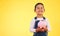 Girl child, piggy bank and saving in studio portrait with smile, mockup space and excited by yellow background. Young