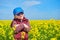 Girl child in rapeseed field with bright yellow flowers, spring landscape