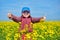 Girl child in rapeseed field with bright yellow flowers, spring landscape