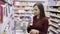 Girl chooses shower gel and sniffs it in cosmetics department at supermarket, emotion dislike