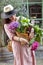 A girl on a city street with a large basket of vegetables and flowers in her hands. Beautiful woman with purchases. Walking along