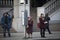 A girl in a claret coat and a grandmother wearing glasses and a claret coat are standing at a bus stop, waiting for the bus