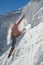 Girl climber climbs a snow cornice using ice axes through snow blown away by the strong wind.