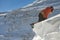 Girl climber climbs a snow cornice using ice axes through snow blown away by the strong wind.